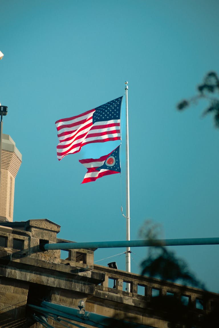 Patriotic display featuring US and Ohio flags waving on a bridge in daylight.